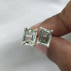 May include: A pair of silver earrings with light green emerald-cut gemstones.