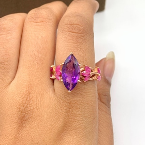 Könnte beinhalten: Ein Ring aus Roségold mit einem großen, markisenförmigen Amethyst-Edelstein, der von kleineren rosafarbenen Edelsteinen umgeben ist.