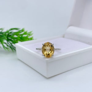 May include: A silver ring with a large oval-shaped topaz gemstone. The gemstone is a light yellow-brown color.