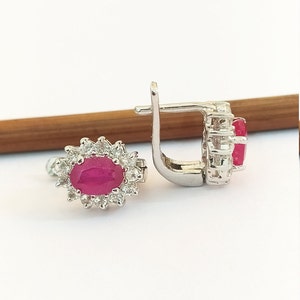 May include: A pair of silver earrings with a red oval gemstone surrounded by smaller white gemstones.