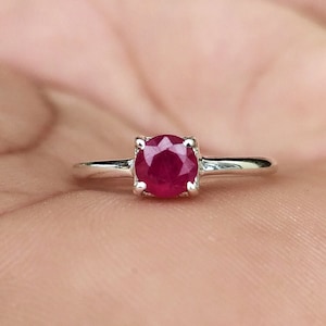 May include: A silver ring with a round, red ruby gemstone.