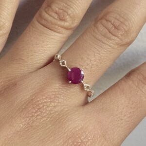 Könnte beinhalten: Ein silberner Ring mit einem runden, tiefrosa Edelstein in der Mitte. Das Band ist mit einer Reihe kleiner, rautenförmiger Metallglieder gestaltet, die vom zentralen Stein ausgehen und ein filigranes und detailliertes Erscheinungsbild erzeugen.