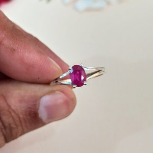 Puede incluir: Un anillo de tono plateado con una piedra preciosa de color rosa intenso de corte ovalado, sujeta por un engaste de cuatro garras. La banda se divide en dos brazos met&aacute;licos finos y pulidos que se unen en la base de la piedra.