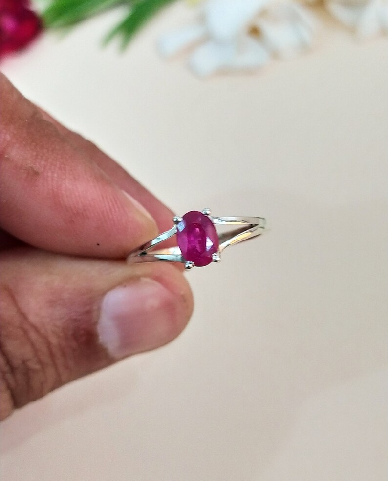 Puede incluir: Un anillo de tono plateado con una piedra preciosa de color rosa intenso de corte ovalado, sujeta por un engaste de cuatro garras. La banda se divide en dos brazos met&aacute;licos finos y pulidos que se unen en la base de la piedra.