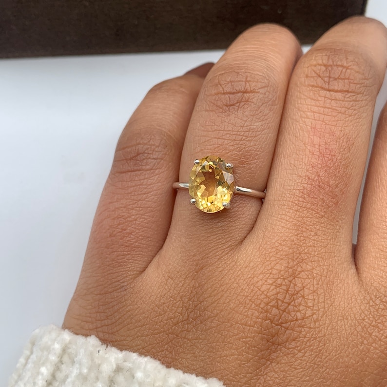 May include: A silver ring with a large oval-shaped yellow gemstone.