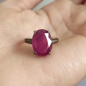May include: A silver ring with a large oval-shaped ruby gemstone. The ruby is a deep red color and has a faceted cut.