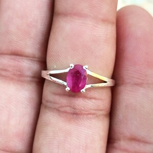 Puede incluir: Un anillo de plata con una piedra preciosa de color rojo rosado vibrante y corte ovalado, sujeta por cuatro garras. La banda presenta un dise&ntilde;o de brazo dividido que se estrecha desde el engaste, creando un aspecto met&aacute;lico pulido.