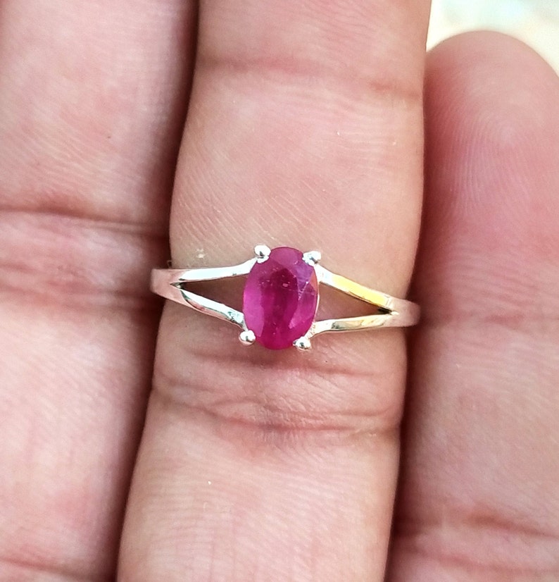 Puede incluir: Un anillo de plata con una piedra preciosa de color rojo rosado vibrante y corte ovalado, sujeta por cuatro garras. La banda presenta un dise&ntilde;o de brazo dividido que se estrecha desde el engaste, creando un aspecto met&aacute;lico pulido.