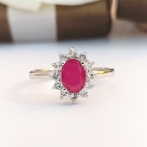 May include: A silver ring featuring a large oval ruby set within a halo of smaller white stones.
