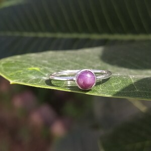 May include: A silver ring featuring a purple star sapphire gemstone.