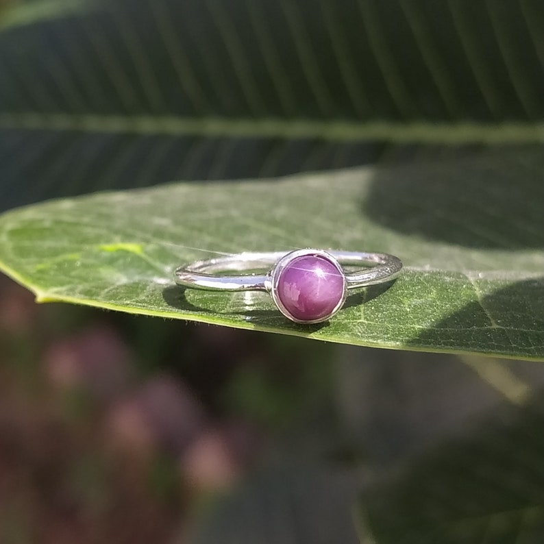 May include: A silver ring featuring a purple star sapphire gemstone.