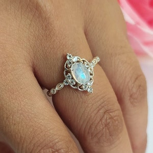 Puede incluir: Un anillo de plata con una gran piedra de luna ovalada y piedras transparentes más pequeñas engastadas en un delicado diseño de filigrana.