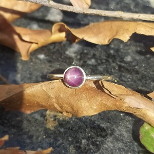 May include: A silver ring featuring a round, purple star ruby gemstone.