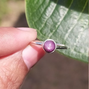 May include: A silver ring featuring a round, purple star ruby gemstone.