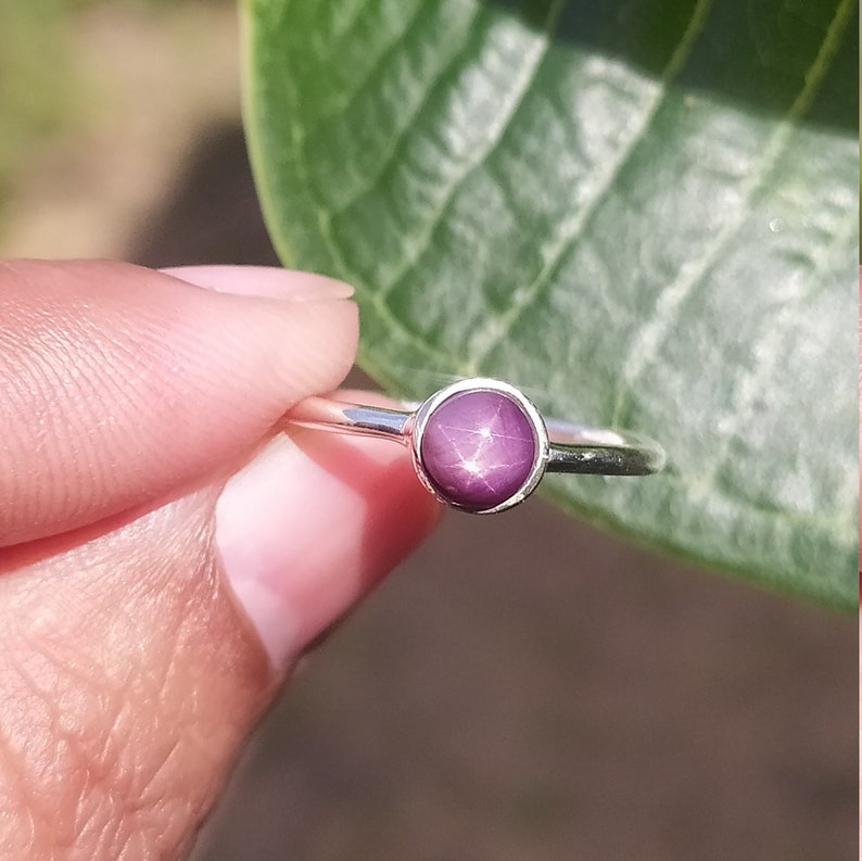 May include: A silver ring featuring a round, purple star ruby gemstone.