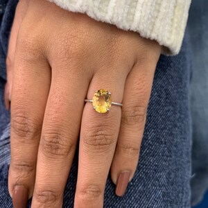 May include: A silver ring with a large oval-shaped yellow gemstone.