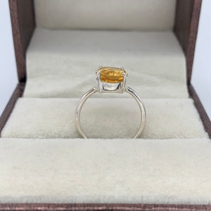 May include: A silver ring with a large, oval-shaped, yellow gemstone set in the center.