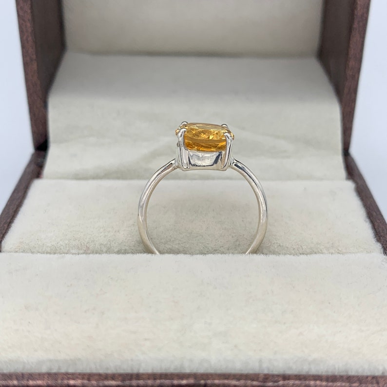 May include: A silver ring with a large, oval-shaped, yellow gemstone set in the center.