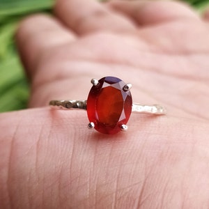 May include: A silver ring with a red oval gemstone. The ring has a hammered texture.