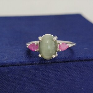 Op de afbeelding: Een zilveren ring met een groene ovale edelsteen en twee roze peervormige edelstenen.