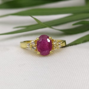 Peut inclure: Une bague en or avec une grande pierre de rubis ovale entourée de petites pierres blanches.