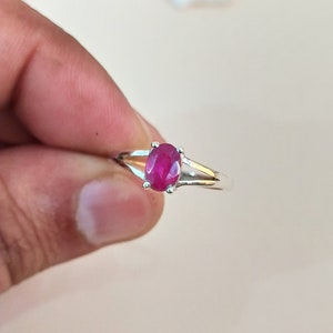 Puede incluir: Un anillo de plata con una piedra preciosa de rubí rosa intenso de corte ovalado, sujeta por un engaste de cuatro garras. La banda del anillo es de plata pulida y presenta un diseño dividido que se estrecha al llegar al engaste.