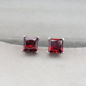May include: A pair of silver stud earrings with square-shaped red gemstones.