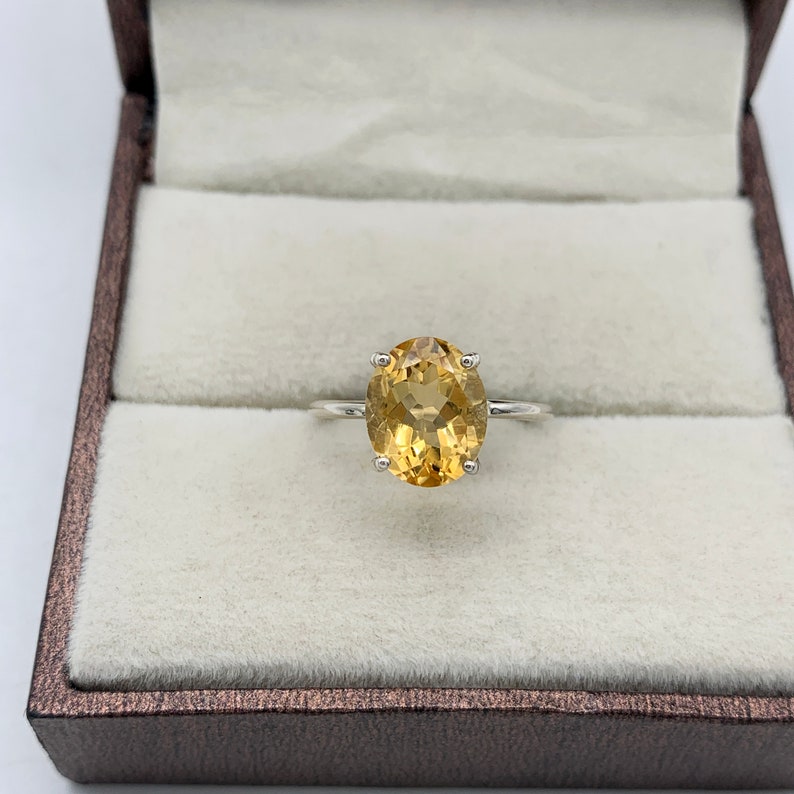 May include: A gold oval-shaped gemstone ring set in a silver band. The ring is displayed in a brown velvet ring box.