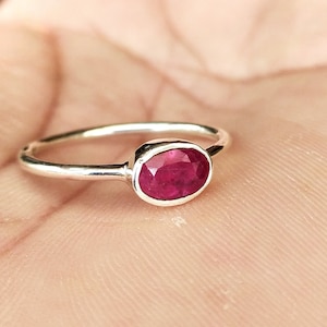May include: A silver ring with a red oval gemstone.
