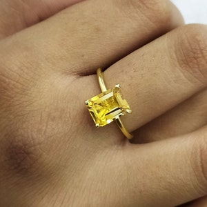 Puede incluir: Un anillo de oro con una gran piedra preciosa amarilla de talla esmeralda.
