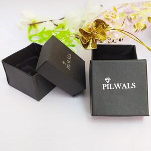 Puede incluir: Dos cajas cuadradas negras para joyer&iacute;a con interiores de terciopelo negro. Las tapas tienen impreso un icono de diamante blanco y el texto PILWALS. Una caja est&aacute; abierta y vac&iacute;a, mientras que la otra est&aacute; cerrada, mostrando la marca arriba.