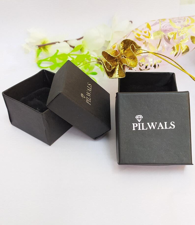 Puede incluir: Dos cajas cuadradas negras para joyer&iacute;a con interiores de terciopelo negro. Las tapas tienen impreso un icono de diamante blanco y el texto PILWALS. Una caja est&aacute; abierta y vac&iacute;a, mientras que la otra est&aacute; cerrada, mostrando la marca arriba.