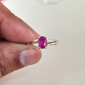Puede incluir: Un anillo de plata con una piedra preciosa de color rojo rosado vibrante y corte ovalado, sujeta por cuatro garras. La banda presenta un dise&ntilde;o de brazo dividido que se estrecha hacia atr&aacute;s, creando un aspecto elegante y pulido.