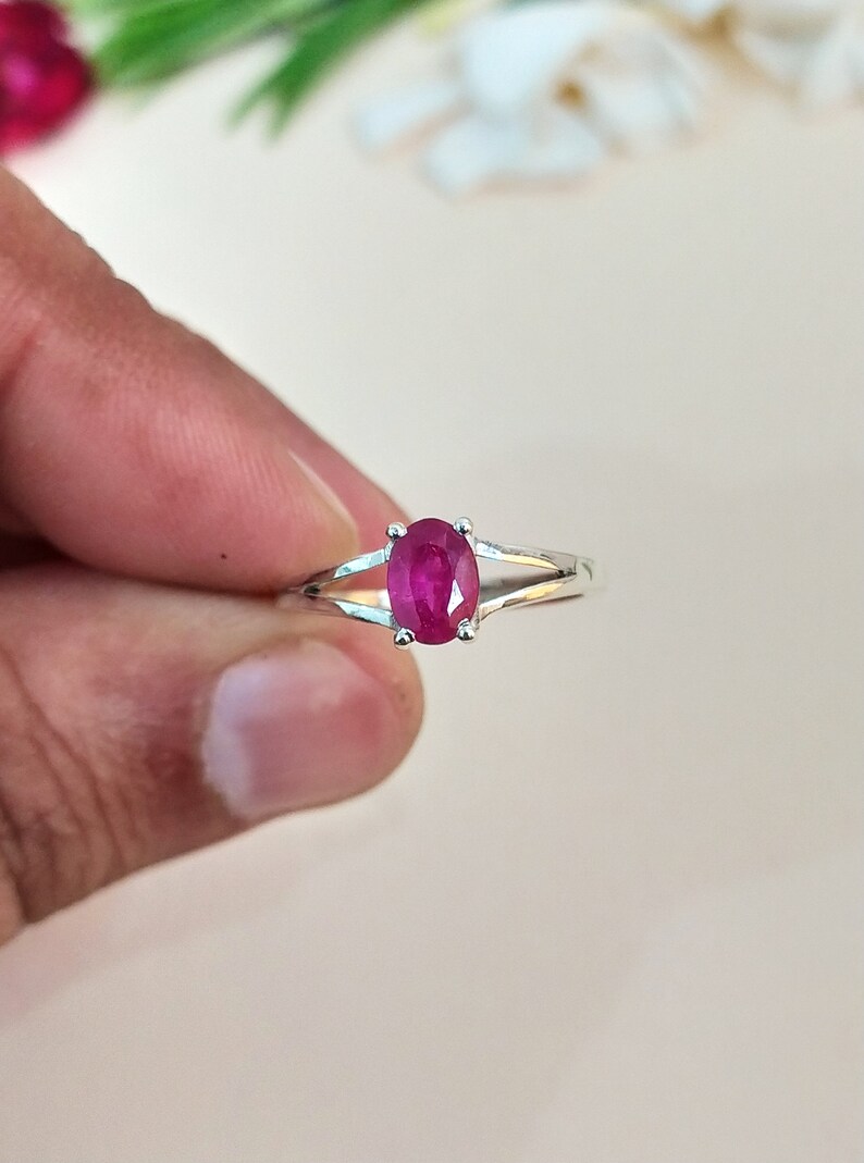 Puede incluir: Un anillo de plata con una piedra preciosa de color rojo rosado vibrante y corte ovalado, sujeta por cuatro garras. La banda presenta un dise&ntilde;o de brazo dividido que se estrecha hacia atr&aacute;s, creando un aspecto elegante y pulido.