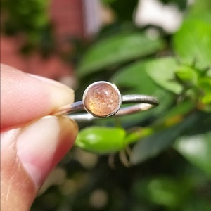 Puede incluir: Un anillo de plata con una piedra redonda de color marrón claro. La piedra tiene un aspecto moteado.