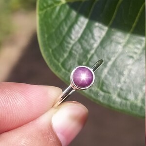 May include: A silver ring with a round, pink star ruby gemstone.