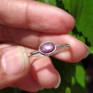 May include: A silver ring with a pink oval star ruby gemstone.