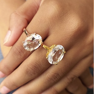 Puede incluir: Dos anillos de oro con piedras preciosas ovaladas transparentes. Los anillos están apilados en un dedo.