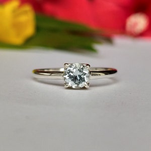 May include: A silver ring with a clear aquamarine gemstone in a prong setting.
