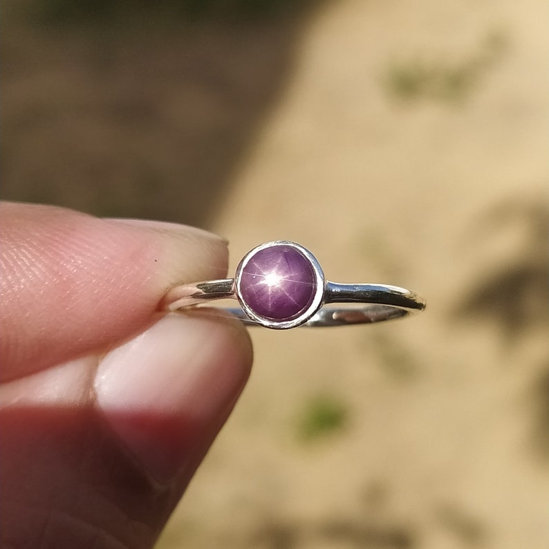 May include: A silver ring featuring a purple star sapphire gemstone. The gemstone displays a star-shaped pattern in its centre.