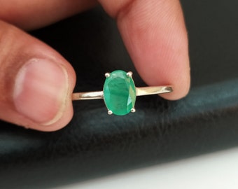 May include: A silver ring with a green oval emerald gemstone.