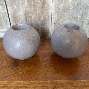 May include: Two gray ceramic candle holders shaped like spheres. The candle holders have a textured surface.