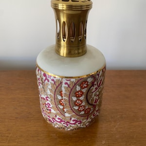 Może przedstawiać: Biały ceramiczny palnik do olejku eterycznego z kwiatowym wzorem w kolorze złotym i różowym oraz mosiężną pokrywką z ozdobnym wzorem.