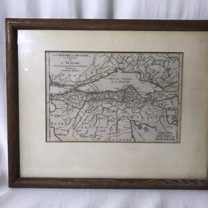 May include: Framed antique map print showing a detailed cartographic depiction of a region, possibly historical. The map is in shades of brown and beige, with text labels. The frame is dark brown wood.