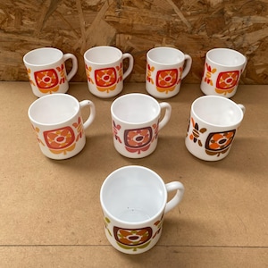Peut inclure: Ensemble de huit tasses en céramique blanche avec un motif floral rétro orange, marron et vert. Chaque tasse a une petite anse et une forme cylindrique. Idéales pour le café ou le thé.