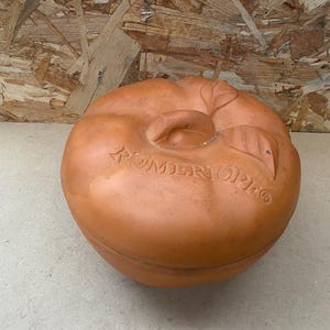 Puede incluir: Un plato para hornear de terracota con forma de manzana con la palabra "Rommertopf" en relieve en el lateral.