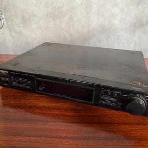 May include: Black Technics stereo amplifier with a silver faceplate and a large knob on the right side. The amplifier has a display screen and several buttons.