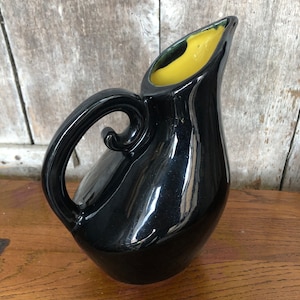 May include: A black ceramic pitcher with a yellow glazed interior and a curved handle.