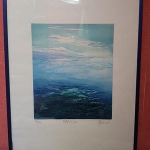 Könnte beinhalten: Gerahmter Kunstdruck mit einer abstrakten Landschaft in Blau- und Grüntönen. Das Kunstwerk ist in einem weißen Passepartout montiert und mit einem dunkelblauen Rahmen versehen. Der Druck ist mit 47/150 nummeriert und enthält handschriftlichen Text und eine Signatur.