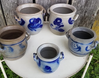 Peut inclure: Cinq pots en céramique bleu et blanc avec des anses. Les pots sont décorés de motifs floraux et géométriques bleus. Les pots sont disposés sur une table blanche avec un fond en bois.